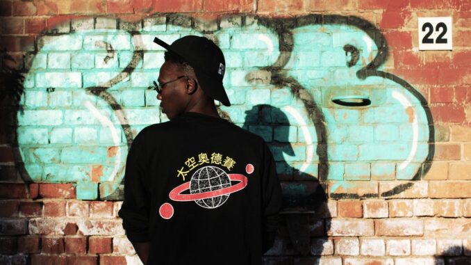 man-wearing-black-long-sleeved-shirt-stands-near-red-wall-1036396