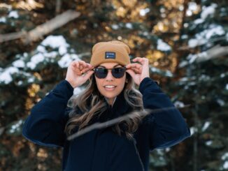 a woman wearing a hat and sunglasses standing in the snow