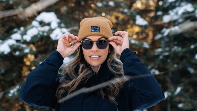 Photo by Karsten Winegeart a woman wearing a hat and sunglasses standing in the snow