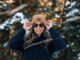 a woman wearing a hat and sunglasses standing in the snow
